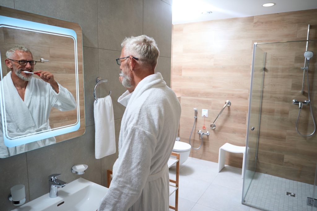 Ein älterer Herr putzt sich im Bad die Zähne