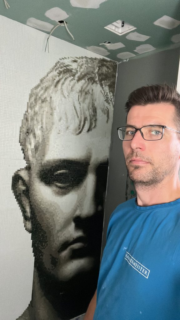 5 frische Ideen für die Gestaltung mit Mosaikfliesen 2 Fliesenleger Benjamin Hammermeister vor einem fertigen Bild-Mosaik in einer Dusche